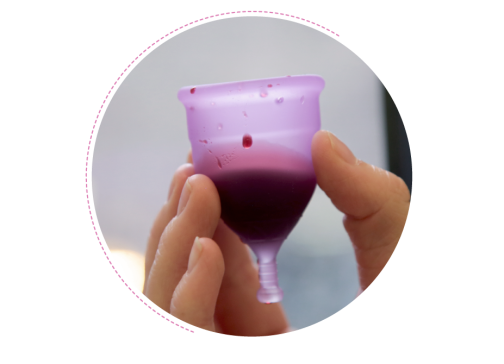 A hand holds a menstrual cup that is filled with blood